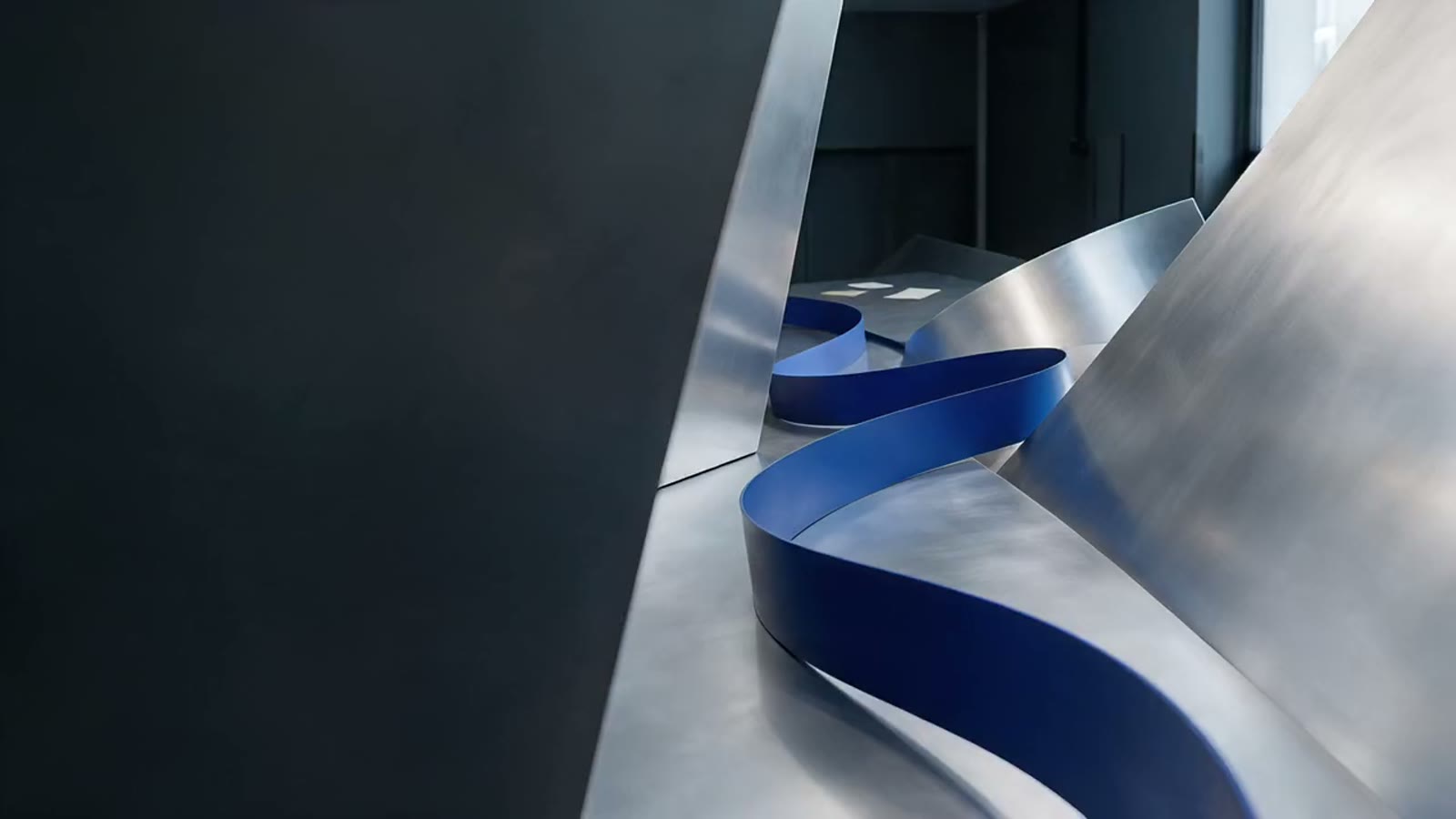A smoothly curved cobalt pathway between aluminium surfaces in soft daylight